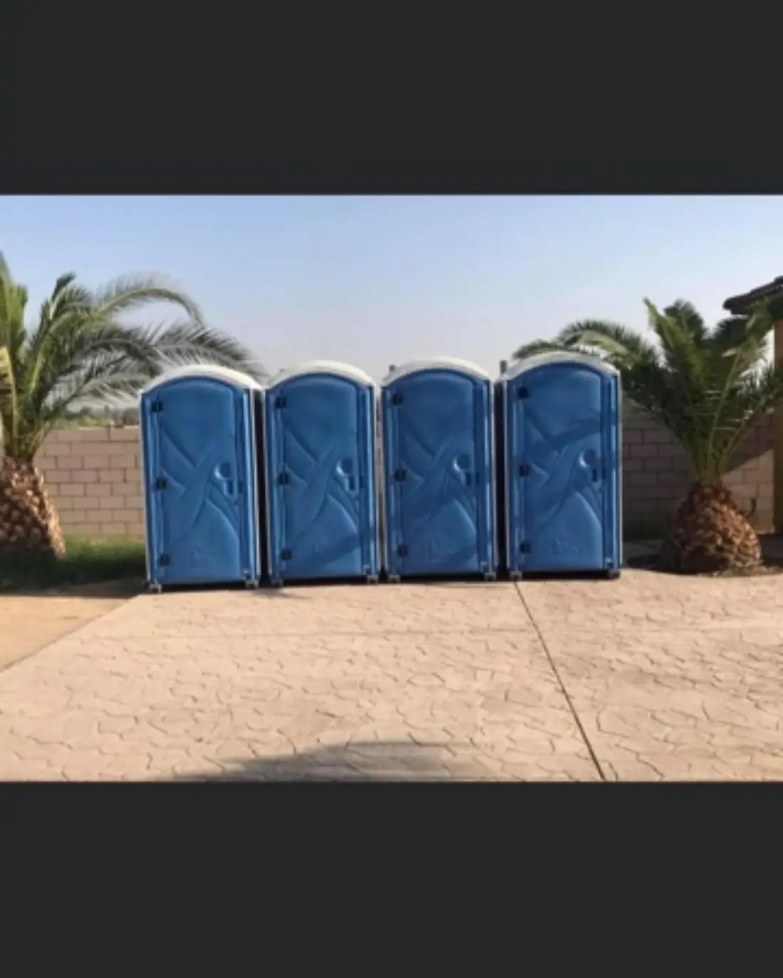Four portable toilets lined up on a concrete pad