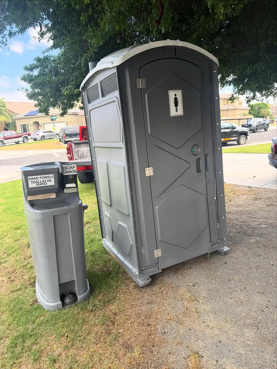 Gray portable toilet with a two-basin hand wash station on grass