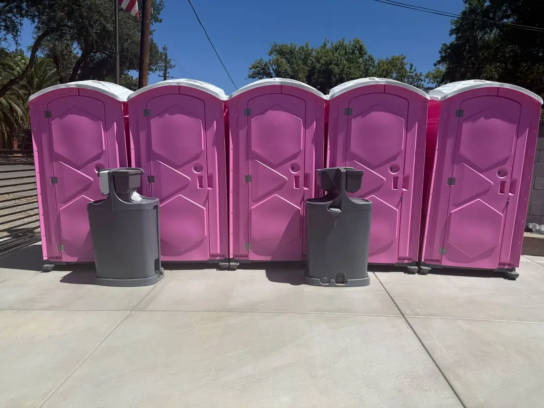 Row of five pink portable toilets with two hand wash stations in front