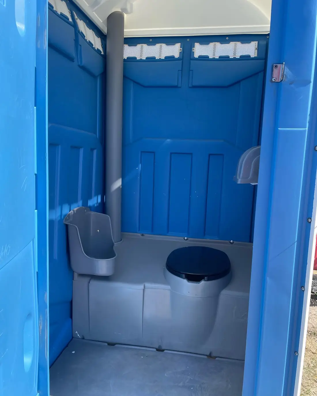 Inside a standard porta potty: seat, toilet paper holders and vent pipe
